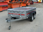 Twin-axle utility trailer with a grey metal body and a tiedown cover, parked in a yard of orange snow plows (Temared Pro).