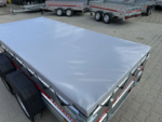 Flatbed trailer with a grey fitted tarp cover, parked among other trailers on a paved lot.