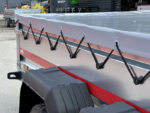 Trailer with a gray tarp secured by black bungee cords along its silver side panel in a loading yard.