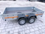 Dual-axle gray metal utility trailer with an orange stripe, empty bed, parked on a paved surface.