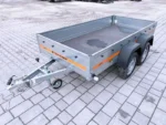 Two-axle utility trailer with gray metal sides and an orange stripe, parked on a paved surface.