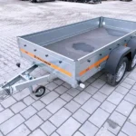 Two-axle utility trailer with gray metal sides and an orange stripe, parked on a paved surface.