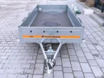 Flatbed utility trailer with gray metal sides and an orange Temared ECO stripe parked on a paved surface, empty bed visible from rear angle.