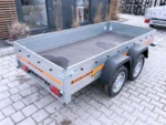 Two‑axle silver utility trailer with orange stripe and Temared branding, parked on a paved lot with an empty bed and gray fenders.