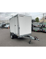 White enclosed cargo trailer on a single-axle chassis with hitch, parked in a lot with other trailers nearby.