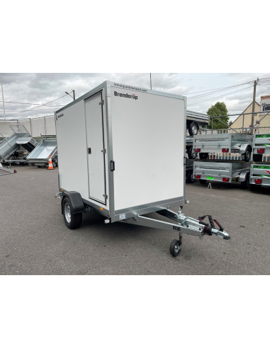 White enclosed cargo trailer on a single-axle chassis with hitch, parked in a lot with other trailers nearby.