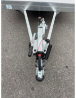 Close-up of a trailer jockey wheel and coupling assembly with handle, spring, and wheel on asphalt surface