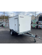White enclosed cargo trailer with a side access door, mounted on a single-axle chassis with a tow hitch and jockey wheel, parked in a lot; brand Brenderup visible on the front corner.