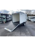 White enclosed cargo trailer with its ramp lowered, parked in a lot among other trailers.