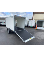 White enclosed cargo trailer with a lowered rear ramp for loading, parked among other trailers.