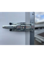 Close-up of a shiny metal door latch securing a white panel to a gray frame, with the bolt engaged.