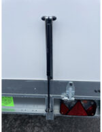 Vertical trailer jack stabilizing the rear of a white trailer, with a metal latch and red taillight nearby