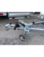 Close-up of a boat trailer hitch with a hand winch, safety chain, and jockey wheel mounted on a galvanized trailer frame.