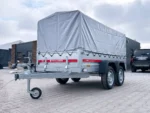 Dual-axle trailer with a gray canvas cover, parked in a paved lot beside a building