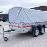 Tow trailer with a large gray tarp covering a cargo area, mounted on two axles with gray metal frame and red Temared branding, parked on a paved lot.